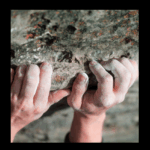 Rock climber griping a rocky surface, with chalky hands.