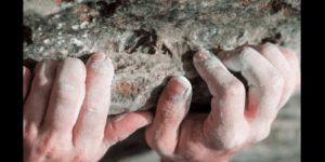 Rock climber griping a rocky surface, with chalky hands.